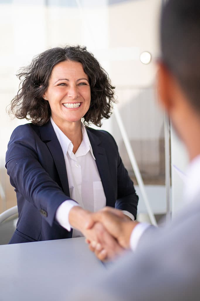 Joyful business woman and man sitting at table, talking and shaking hands